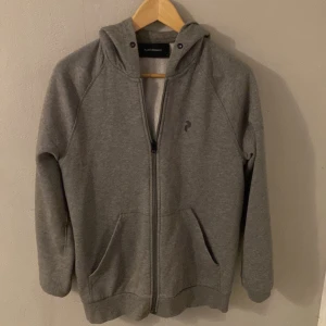 Grå hoodie med dragkedja - Säljer en stilren grå hoodie från Peak performance . Tröjan har en praktisk dragkedja framtill och en bekväm huva. Perfekt för en avslappnad look. Men har inte kvar snörenrna på tröjan.