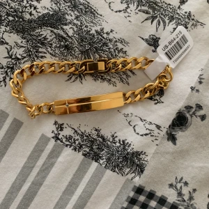 Guldarmband  - Snyggt guldarmband i rostfritt stål med en stilren design. Armbandet har en platt mittdel och en robust kedja med ett säkert lås. Perfekt för att ge en elegant touch till din stil.