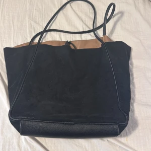 Svart och brun axelväska från H&M - Snygg och rymlig axelväska från H&M i svart och brunt. Väskan har en stilren design med långa axelremmar och en praktisk öppning. Perfekt för att bära med sig allt man behöver under dagen.