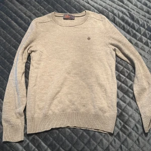 Beige tröja från Morris - Säljer en stilren beige tröja från Morris Stocholm  med rund hals och ett diskret broderat emblem på bröstet. Tröjan har långa armar. Den har krympt och sitter därför som XS. 100 procent % Merino wool. 