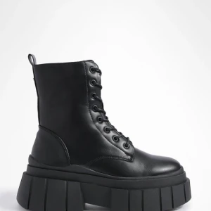 Chunky, Platå kängor - AI-beskrivning; Snygga svarta boots med kraftig platåsula och snörning. De har en dragkedja på sidan för enkel på- och avtagning. Perfekta för att ge din outfit en edgy touch. 