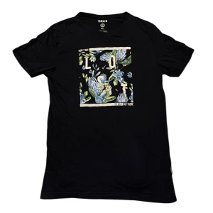 Svart t-shirt med blommigt tryck från Solid - Snygg svart t-shirt från Solid med ett färgglatt blommigt tryck på framsidan. Perfekt för en avslappnad stil. Tillverkad i mjukt material för extra komfort.