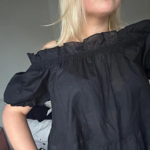 Svart offshoulder blus - Säljer en svart offshoulder blus med korta ärmar och elastisk kant vid axlarna. Helt oanvänd med lappen kvar! Skitsnygg till sommaren🥰🥰