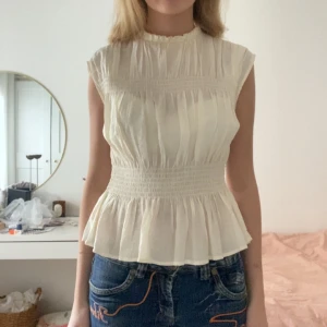 Vit blus med smockdetaljer - Säljer en söt vit blus med smockdetaljer i midjan och volang . Inga defekter!!