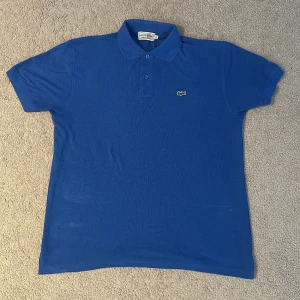 💫Blå pikétröja från Lacoste💫 - Nyligen köpt från en vintage butik och har ej testat om den svaga fläckarna går att tvätta bort, dock märker man ej av dem när tröjan sitter på. Vid mer info/bilder skriv priv.