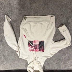 Vit hoodie från Moncler  - Riktigt unik, Säljer en snygg vit hoodie från Moncler med ett coolt tryck i rosa och svart på framsidan. Hoodien har en justerbar huva med vita snören och en ficka framtill. Perfekt för en avslappnad stil. Passar mindre 