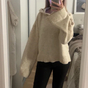 Beige stickad hoodie - Mysig beige stickad hoodie med långa ärmar och ribbade muddar. Perfekt för kyliga dagar när du vill ha något bekvämt och stilrent. Den har en avslappnad passform och en stor huva för extra värme.