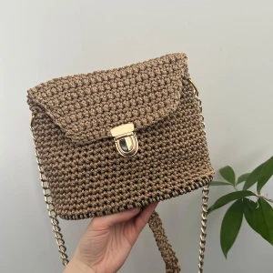 Handmade Beige stickad axelväska med kedja - Snygg beige stickad axelväska med guldfärgad kedja och spänne. Perfekt för att ge en trendig touch till din sommar outfit. Väskan har en unik stickad design som gör den både stilren och iögonfallande. Handmade av min mamma💝