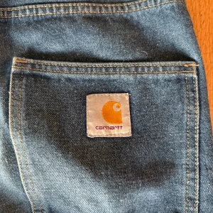 Blå jeans från Carhartt - Säljer ett par klassiska blå jeans från Carhartt. De har en rak passform och är tillverkade i slitstarkt denim. Byxorna har fem fickor och en knappgylf. Perfekta för en avslappnad stil. Storleken säger M, den passar mig som vanligtvis har 32/32. 