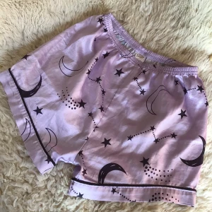 Lila shorts med stjärnmönster - Säljer ett par lila shorts från Oyo med ett coolt mönster av stjärnor och månar. De har en elastisk midja för extra komfort och är perfekta för en avslappnad look. Materialet känns mjukt och skönt mot huden.