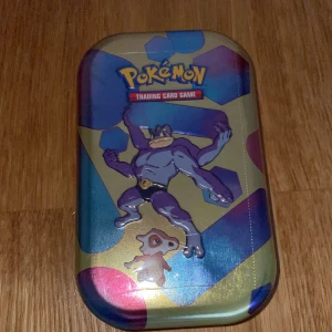 Pokémon Trading Card Game Mini Tin 151 made in USA - Säljer en Pokémon Trading Card Game Mini Tin med motiv av Machamp och Cubone. Perfekt för att förvara dina kort eller som samlarobjekt. Tinnet har en färgglad design med holografiska detaljer.