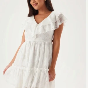 Vit klänning med volangdetaljer - Säljer en söt vit klänning med volangdetaljer och v-ringning. Klänningen har en luftig passform och är perfekt för sommarens varma dagar. Den är ärmlös och har en kort längd som ger en lätt och ledig känsla. Säljer två stycken i två storlekar då jag köpt en annan klänning. 