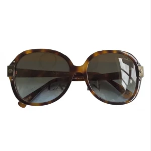 Solglasögon från Lanvin - Snygga solglasögon från Lanvin med en klassisk rund form och ett trendigt sköldpaddsmönster. Bågarna har en brun nyans och glasen är mörka för att skydda mot solen. Perfekta för en stilren look.