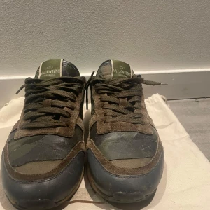 Valentino Rockrunner i kamouflage - Snygga Valentino Rockrunner sneakers i en cool kamouflagefärg. Skorna har en mix av gröna och bruna toner med svarta detaljer. De är tillverkade i en kombination av skinn och mocka, och har klassisk snörning. Perfekta för en trendig look. Säljer dessa då de är för små för mig. Bara att kontakta mig för minsta fråga.