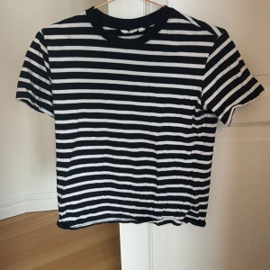 Svartvit randig t-shirt - Säljer en klassisk blåvit randig t-shirt i bomull. Den har en normal passform och korta ärmar, perfekt för en avslappnad stil. T-shirten är tillverkad i Bangladesh och är superbekväm att bära.