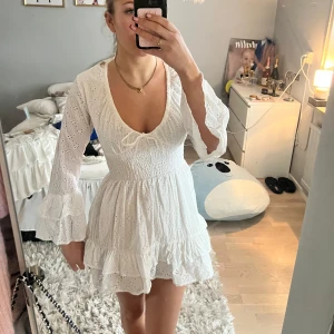 Vit klänning från Boux Avenue - Säljer en söt vit klänning från Boux Avenue med broderade detaljer och volanger. Klänningen har långa ärmar och en v-ringad design med knytning framtill. Perfekt för studenten! 🌸köpte denna i london🤍