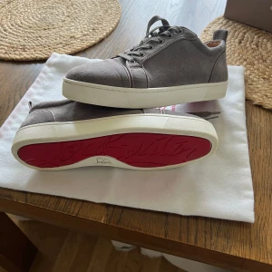Louboutin skor - Snygga grå sneakers i mocka från Christian Louboutin med den ikoniska röda sulan. Skorna har snörning och en vit gummisula som ger en stilren look. Perfekta för dig som vill ha något exklusivt och trendigt.