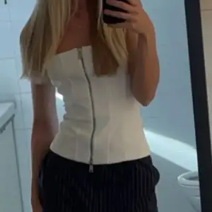 Snygg vit tubtopp med dragkedja framtill. Perfekt för en stilren look, kan matchas med både jeans och kjol. Enkel och chic design som passar till många tillfällen.