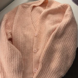 Rosa stickad kofta från NA-KD - Mysig rosa stickad kofta från NA-KD med v-ringning och knappar framtill. Perfekt för kyliga dagar när du vill ha något bekvämt och stilrent. Koftan har långa ärmar och en mjuk textur som ger en skön känsla.