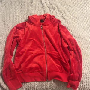 Röd, mjuk hoodie med dragkedja - Säljer en mjuk och bekväm röd hoodie med dragkedja framtill. Hoodien har långa ärmar och ribbade muddar vid ärmslut och nederkant. Perfekt för en avslappnad stil. Lite använd. 95% Polyester, 5% Elastan. 