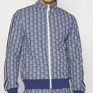 Blå mönstrad jacka från Lacoste - Säljer en blå mönstrad jacka från Lacoste med dragkedja framtill.  
