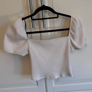 Vit ribbad topp med puffärmar - Säljer en söt vit ribbad topp med puffiga kortärmar. Toppen har en fyrkantig halsringning och är perfekt för en stilren look. Passar bra till både jeans och kjol.