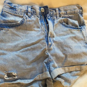 Blå jeansshorts från Topshop - Säljer ett par  blå jeansshorts från Topshop med slitna detaljer. Shortsen har hög midja. 