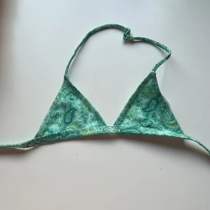 Grön bikiniöverdel från Gina Tricot - Mintgrön trekantsbikini från Gina. Det är storlek 134/140. Tricot med paisleymönster i grönt, blått och inslag av gult. Klassisk modell med knyt i nacken och under bysten. Perfekt för strandhäng och pooldagar.