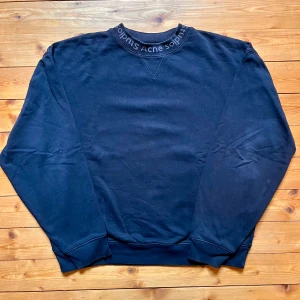 Svart sweatshirt från Acne Studios - Svart sweatshirt från Acne Studios med logotypen broderad runt kragen. Klassisk passform med ribbade muddar och rund hals. Perfekt basic med stilren design och diskret branding. Tillverkad i mjuk bomull för maximal komfort. Tröjan är väldigt oversized