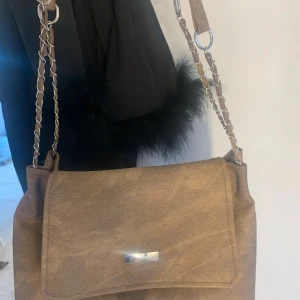 Brun axelväska från Mixxen - Säljer en snygg brun axelväska från SHEIN med kedjedetaljer på axelremmen. Finns inga fack i väskan!