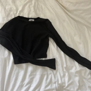 Svart croppad långärmad tröja - Svart croppad långärmad tröja. Tröjan är ribbad och har en tight passform med rund halsringning. Perfekt att styla med höga jeans eller kjol för en clean look.