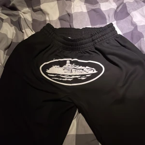 Svarta mjukisbyxor med tryck, M - Svarta mjukisbyxor med vit snörning i midjan och stort vitt tryck framtill. Byxorna har elastisk midja och en bakficka. Materialet känns mjukt och bekvämt, perfekt för chill dagar. Snygg och enkel design med unik grafisk detalj.