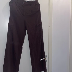 Bruna cargopants med vida ben - Säljer ett par bruna cargopants med bred passform och stora fickor på sidorna. Byxorna har normal midja och raka, vida ben. Perfekta för en avslappnad och trendig stil.