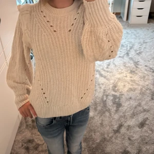 Beige stickad tröja med volang från Vila - Superfin beige stickad tröja från Vila med volangdetaljer på axlarna och snygga hålmönster framtill. Perfekt för höst, vår och vinter. Använd minst en gång och inga tecken på användning. 