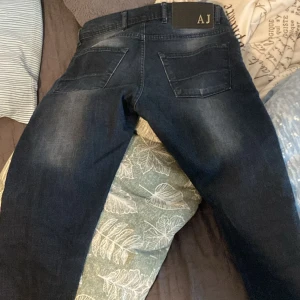 Mörkblå Armani Jeans, storlek 30 - Snygga mörkblå jeans från Armani Jeans med klassisk femficksdesign och AJ-logga på bakfickan. Jeansen har en lätt tvättad look och raka ben. Tillverkade i mjukt jeanstyg som sitter skönt hela dagen.