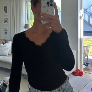 Svart ribbad topp med spets från SHEIN - Svart långärmad topp från SHEIN i ribbad bomullsmix med v-ringning och spetskant. Sitter tight och har en snygg rynkdetalj vid bysten. 