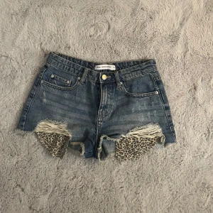 Jeansshorts med leoparddetaljer Sinsay - Snygga blå jeansshorts från Sinsay med råa kanter och slitningar framtill. Fickorna har coolt leopardmönster som sticker fram under de trasiga partierna. Klassisk femficksmodell och knappstängning. Perfekta för dig som vill ha en classics och fin look!🤍🤍