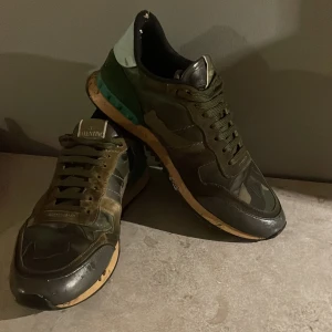 Valentino Rockrunner sneakers camouflage - Snygga Valentino Rockrunner sneakers i grönt och brunt med coolt camouflage-mönster. Skorna har snörning, platt sula och detaljer i skinn och mocka. Perfekta för dig som vill sticka ut med exklusiva och trendiga sneakers.