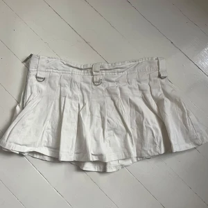 Vit minikjol med insydda shorts från The Kript - Superfin vit plisserad minikjol från The Kript med coola D-ringar och dragkedja i sidan. Kjolen har bälteshällor och en snygg, lite sportig vibe. Perfekt för dig som gillar trendiga och stilrena plagg. Har insydda shorts under så funkar att ha även fast den är kort. Köpt på sellpy men aldrig använd. Men är i bra skick från när jag fick den🩷