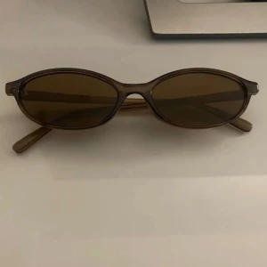 Bruna solglasögon - Säljer snygga solglasögon med smala, ovala bågar i transparent brun plast och matchande bruna glas. Perfekt accessoar för en cool och retro look. Lätta och bekväma att bära hela dagen.