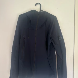 Svart vindjacka från C.P. Company - Snygg svart pro-tek vindjacka från C.P. Company med huva och dragkedja framtill. Jackan har logga på ärmen, praktiska fickor med dragkedja och justerbara ärmslut. Perfekt för dig som vill ha en stilren och funktionell jacka till vardags. Vid mer frågor eller funderingar är det bara att skriva. OBS: Skickas ej! Hämtas/möts i Kållered/Mölndal/Göteborg. Mvh I.