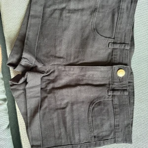 Svarta jeansshorts - Snygga svarta jeansshorts med klassisk femficksdesign och gylf med knapp. De har bälteshällor och raka ben, perfekta för en chill sommarlook. Passar dig som gillar enkel och stilren vibe.