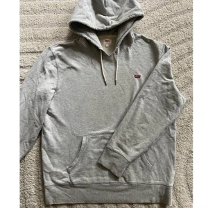 Grå hoodie från Levi's  - Snygg grå hoodie från Levi's med luva och vita snören. Tröjan har en ficka framtill och liten röd Levi's-logga på bröstet. Säljer då den inte används länge, har inga defekter eller liknade 🥰🥰första bild lånad!