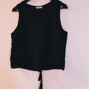 Svart ärmlös topp från ONLY strl 38 - Svart ärmlös linnetopp från ONLY med rund halsringning och knytning nertill. Toppen har en öppen detalj i ryggen som ger en snygg twist. Perfekt till jeans eller kjol för en clean look.  Helt & fint skick