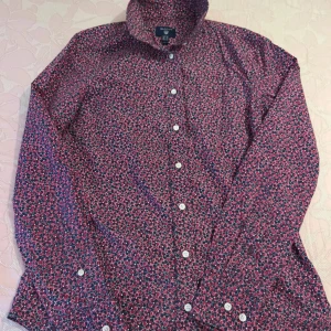 Blommig skjorta från GANT, röd/blå - Snygg skjorta från GANT med blommigt mönster i rött, blått och vitt. Skjortan har lång ärm, klassisk krage och vita knappar framtill. Perfekt för dig som vill sticka ut med färg och mönster. Tillverkad i mjuk bomull för en skön känsla. Pris kan diskuteras. 