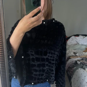 ❤️ - Säljer en svart, pälsig sjal med cool struktur och pärldetaljer längs halsringning, ärmar och nederkant. Tröjan har vida ärmar och känns riktigt mjuk och lyxig. Perfekt för dig som vill sticka ut med en unik och trendig look.