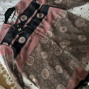 Mönstrad skjorta från B*B i brunt och rosa - Unik skjorta från B*B med detaljerat blommigt mönster i bruna, rosa och svarta toner. Långärmad modell med knappar framtill och mjukt, tunt tyg som känns luftigt. Perfekt för dig som gillar bohemiska vibes och snygga detaljer.