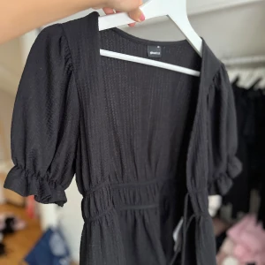 Svart topp från Gina Tricot - Supersöt svart topp från Gina Tricot med puffärmar och markerad midja. Klänningen har en lätt struktur i tyget och volangdetaljer vid ärmsluten. Perfekt för dig som gillar en feminin och trendig stil.