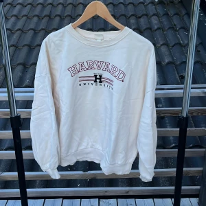 Vit Harvard sweatshirt från H&M - Vit sweatshirt från H&M med Harvard University-tryck i vinrött och svart framtill. Tröjan har rund hals, ribbade muddar och en relaxed passform. Perfekt för dig som gillar college-vibe och oversized stil.