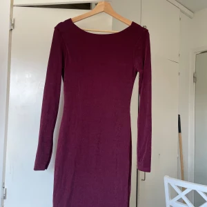 Vinröd långärmad klänning Gina Tricot - Vinröd kortklänning med lång ärm och snygg draperad öppen rygg. Klänningen är figurnära och har en mjuk, lätt glansig yta. Perfekt för dig som vill sticka ut med en elegant men enkel look.